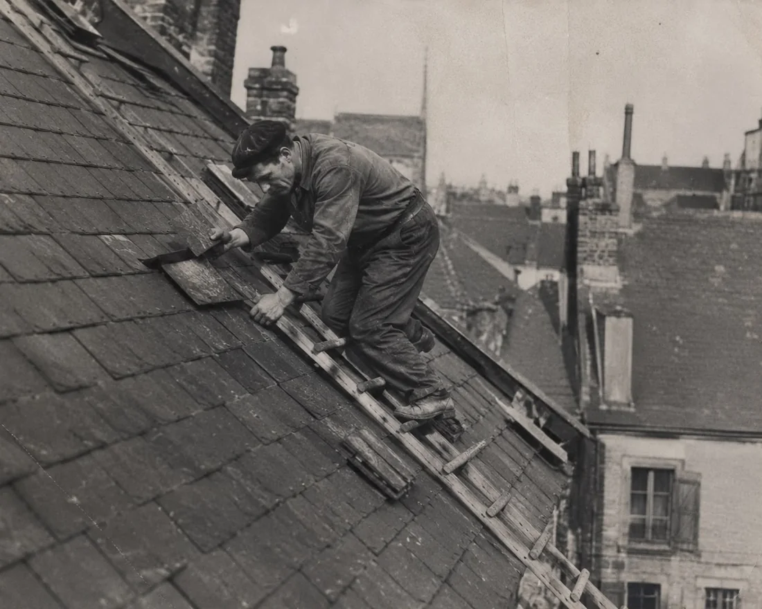 Couvreur à l’ouvrage sur une toiture en ardoise, photographie d’archive du métier