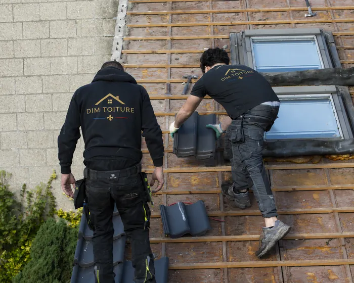 Deux couvreurs de Dim Toiture posant des tuiles sur liteaunage autour de fenêtres de toit